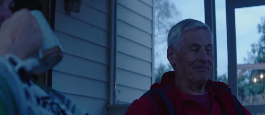 Two elderly people drinking from a mug sitting on the porch talking