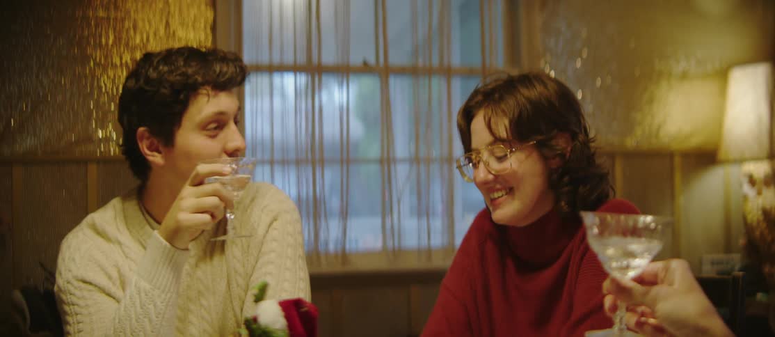 Two people laugh and drink from martini glasses at a holiday gathering