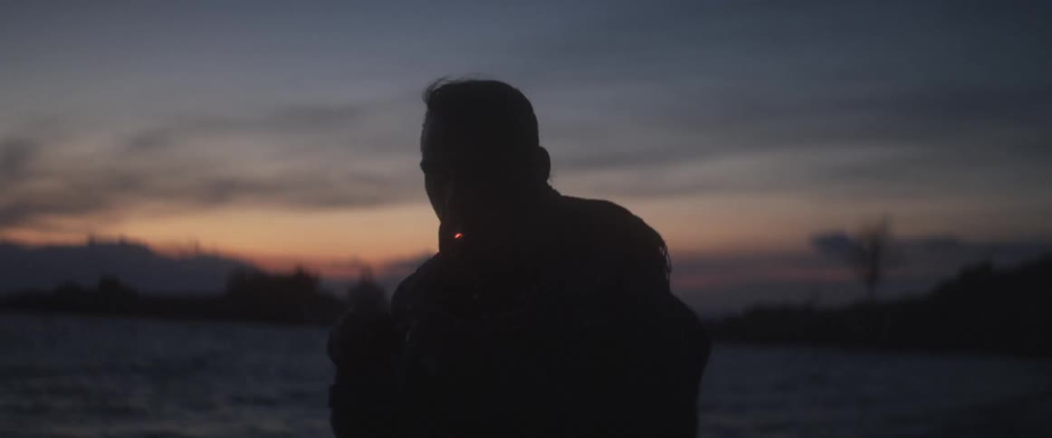 A man smokes a cigarette on a beach at dusk