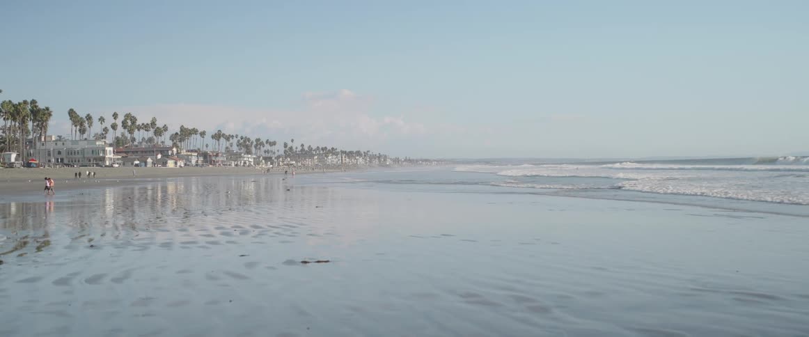 The damp sand on the edge of a beach with the sea on the right and the coast on the left