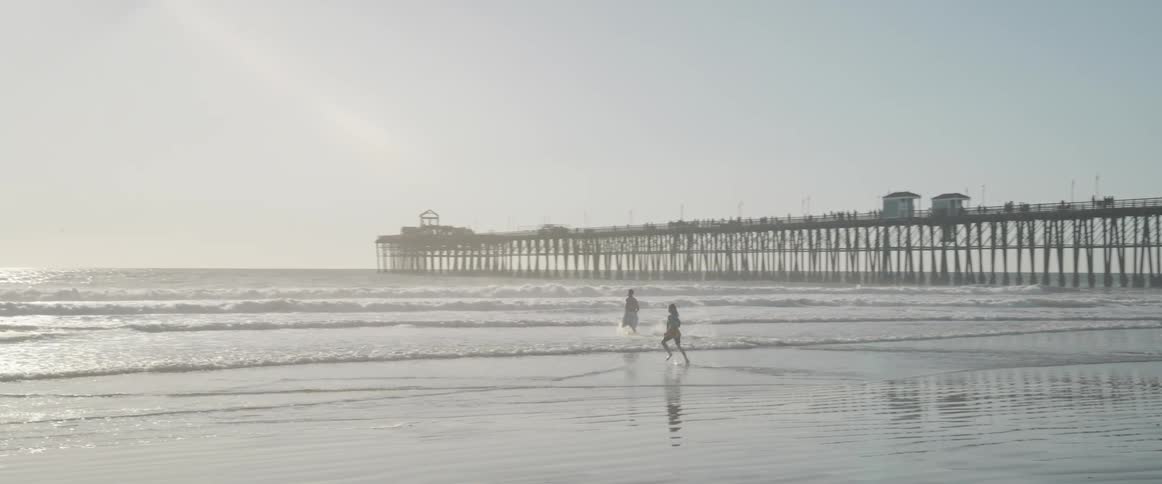 Two people running on the sand towards the sea