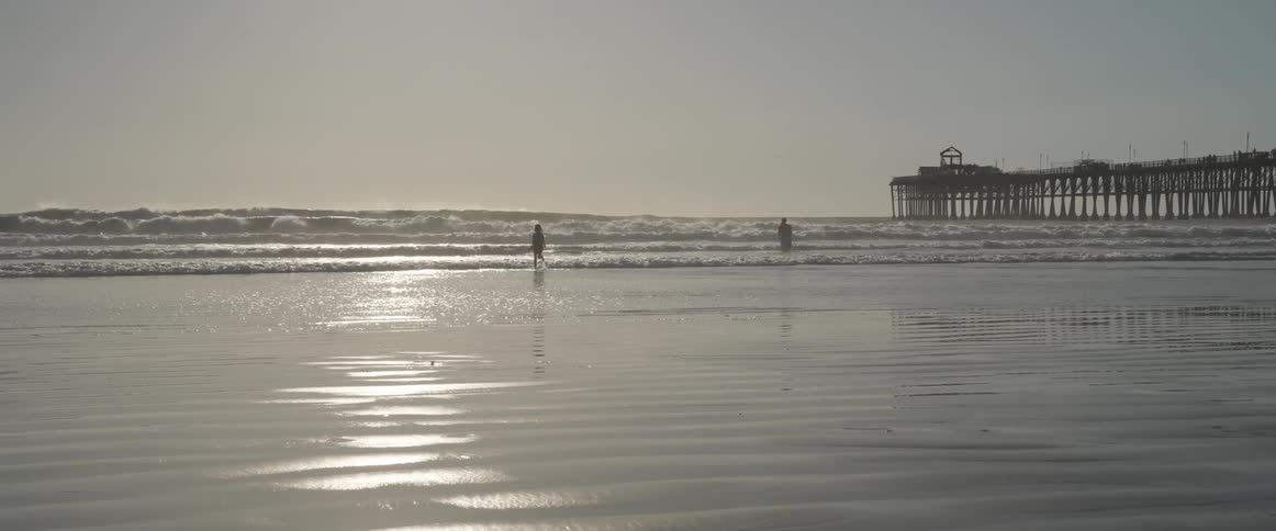 Three people having fun in the sea with a pier in the background