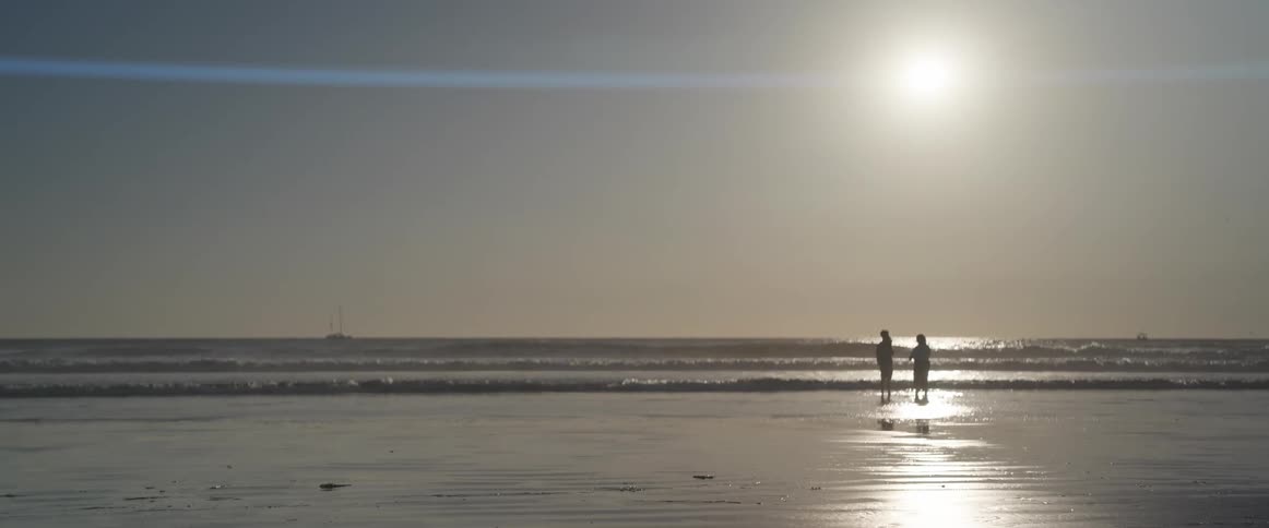 The silhouette of two people on the shore of the sea water of a beach in the morning
