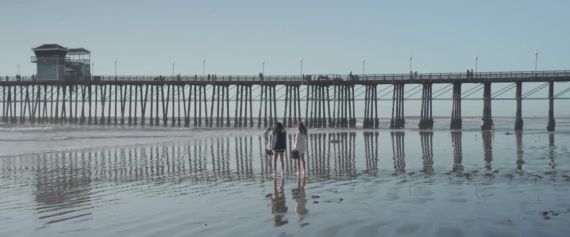 Two women on the wet sand of the beach next to a pier