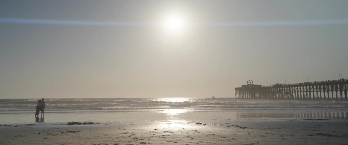 Two people on the sand on the beach facing the sea with the sun in the background