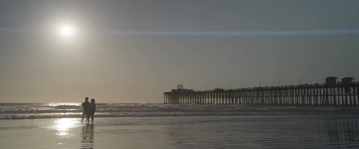 Two people on the sand of the beach with the sea and the sun in the background