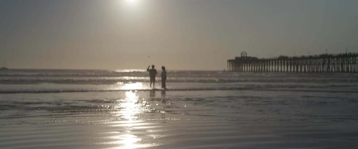 Two people in the sea on the beach with the sun in the background