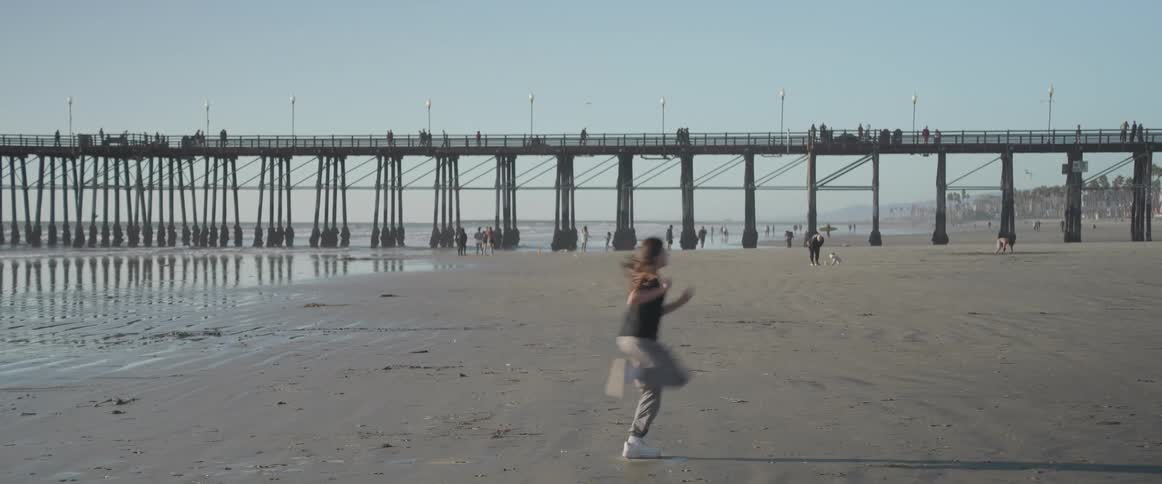 Person running on the beach with a pier in the background