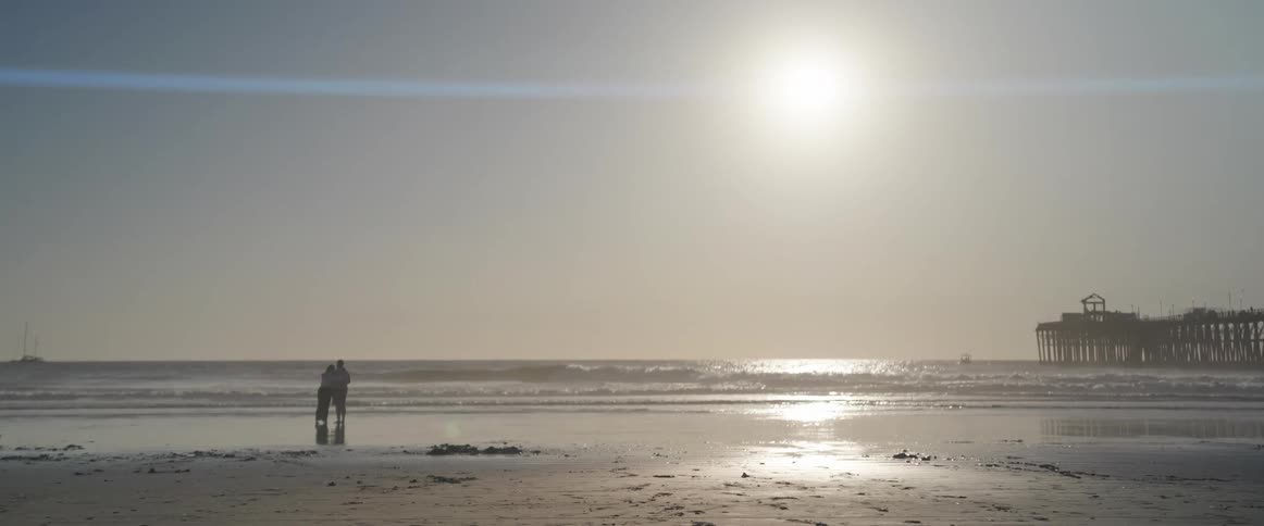 People on the sand of the beach with pier in the background
