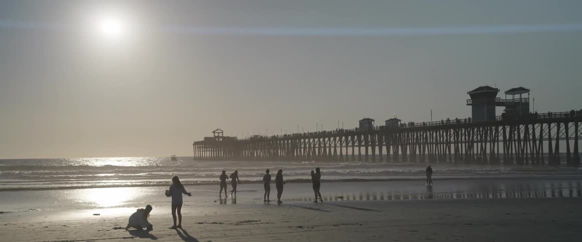 People walking on the sand of the beach and a pier in the background