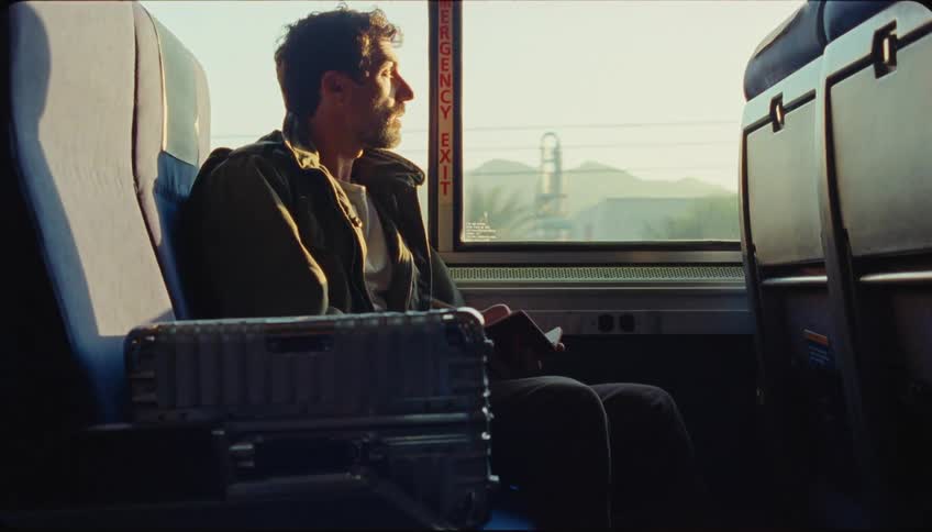 A man sitting on a seat of a public vehicle and he is writing something in a notebook and then he looks out the window