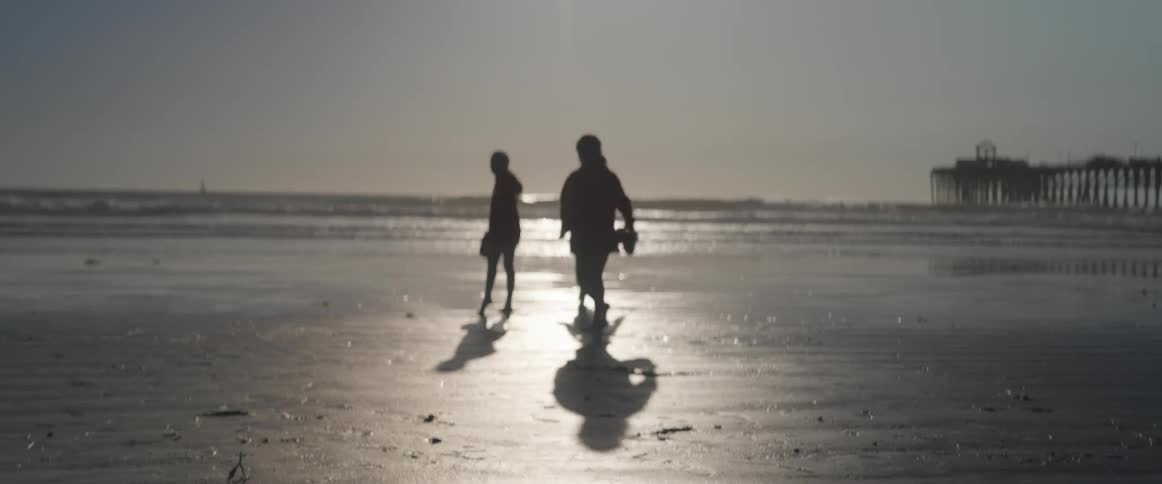 Children running on the beach with a pier in the background