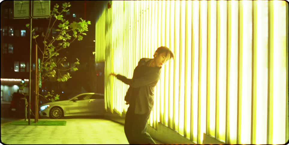 Man dancing a performance on a sidewalk at night next to a bright building