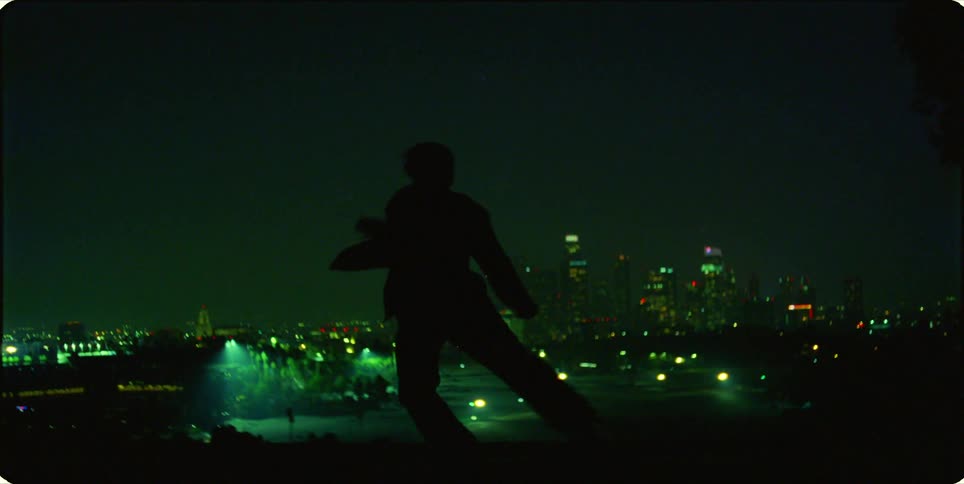 The silhouette of a man dances with a city behind him lit up at night