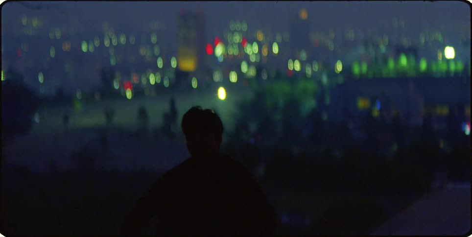 A man dances in the dark with a bright city behind him