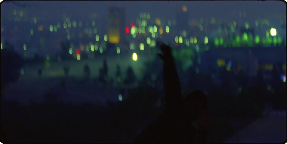 Silhouette of a person dancing outdoors with a city in the background lit up at night