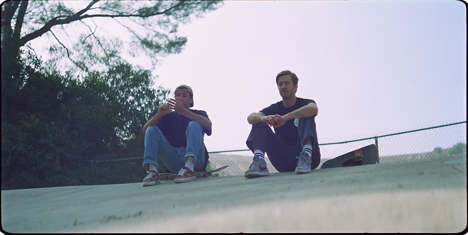Two young men sitting with a skateboard talking outdoors
