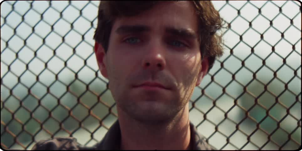 Man standing emotionless in front of an outdoor fence