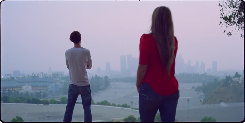 Woman joins man standing on a hill and looking towards the foggy city skyline