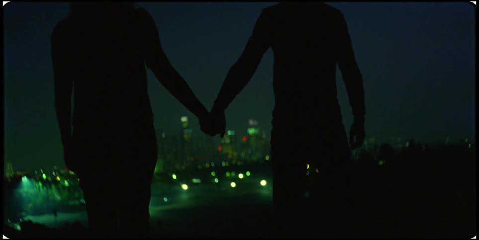 Silhouette of two people holding hands with a panoramic view of an illuminated city at night