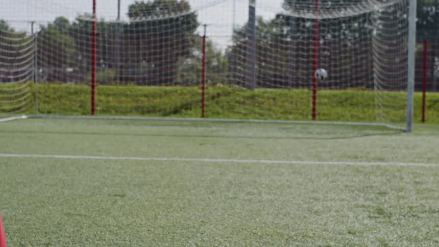 A soccer player kicks a ball into a goal net on a summer day