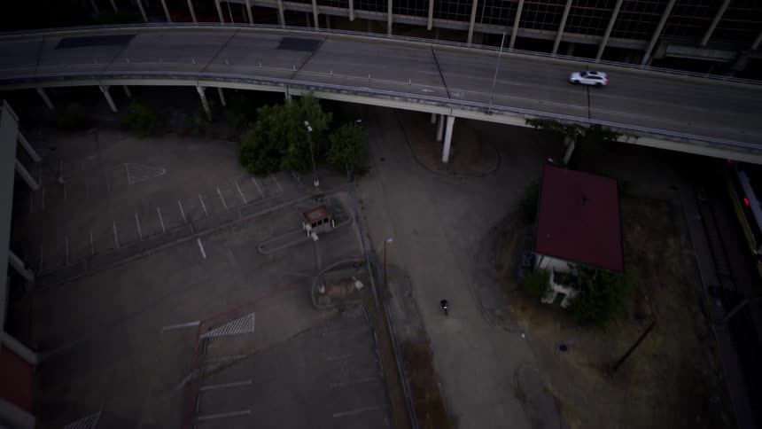 Aerial view of a motorcycle moving through narrow streets below an overpass