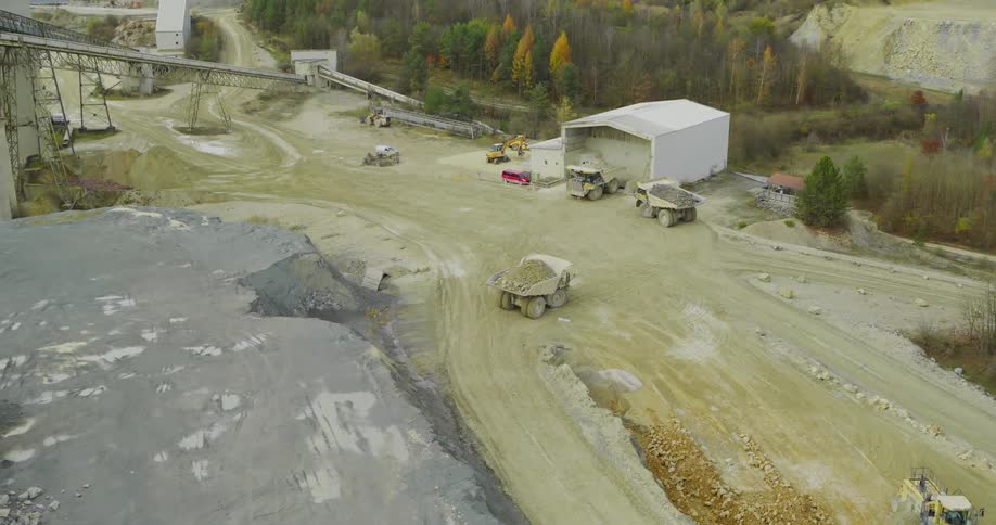 An aerial view of an active quarry with large mining trucks and machinery operating in a vast dusty landscape