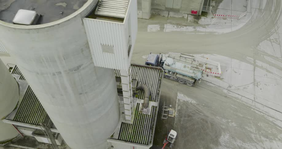An aerial view of a large industrial site with a tall silo several trucks and a complex network of pipes and machinery