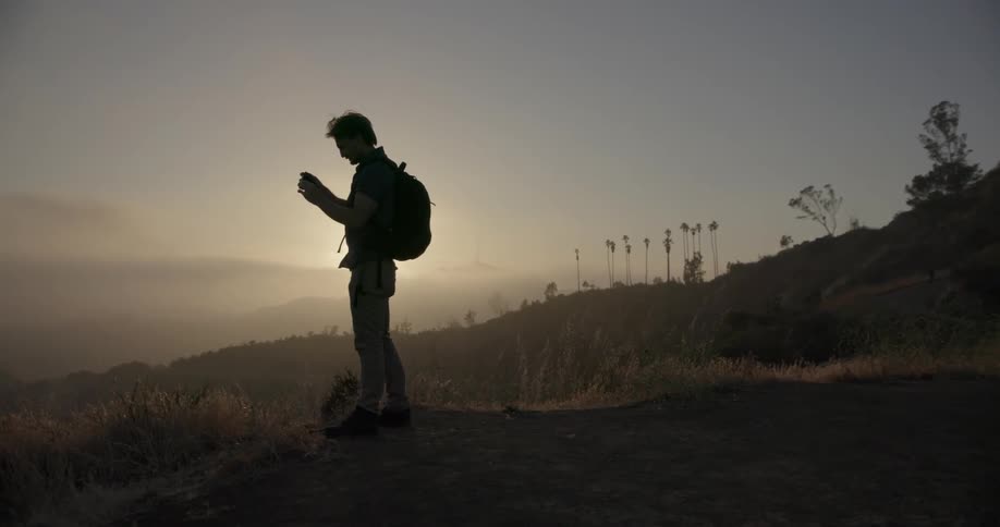 A hiker is stopping at sunrise to look through binoculars