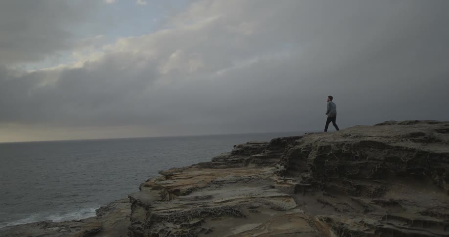 A man standing on an ocean cliff on an overcast day
