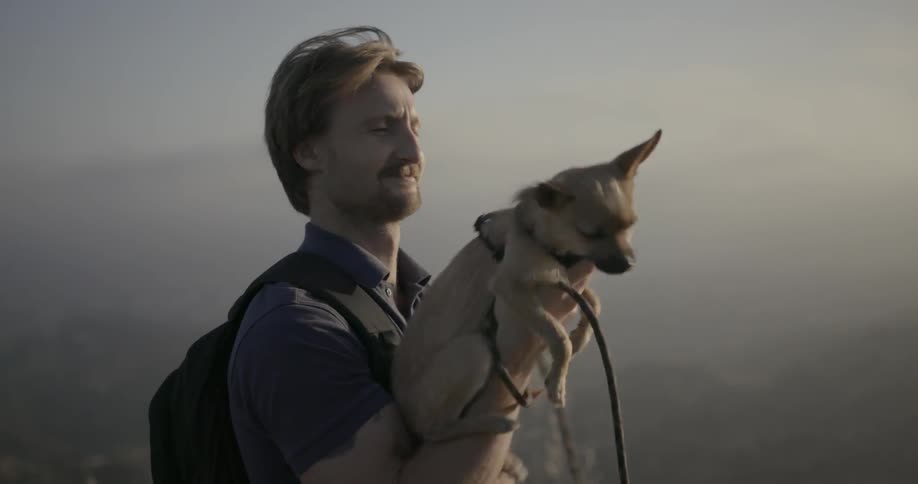 A man holding a small dog up and then pulling it close to him