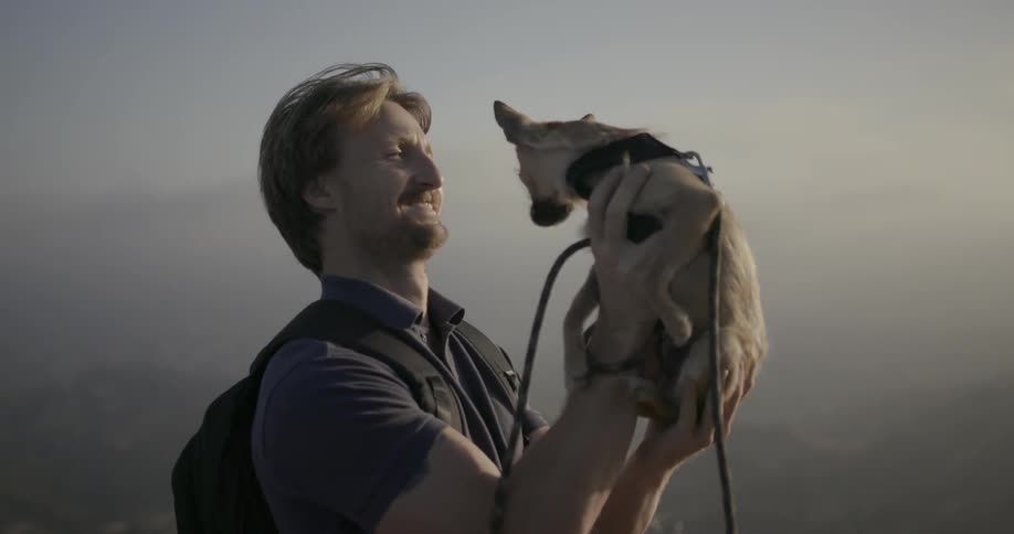 A man is holding up a tiny dog and smiling