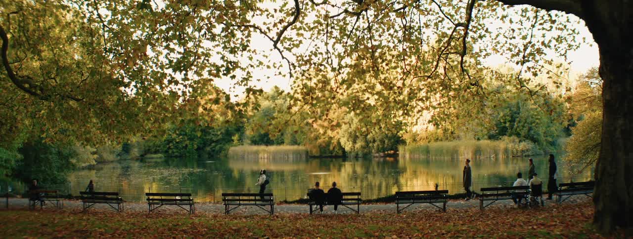 A serene park scene with a lake people relaxing on benches and a canopy of golden autumn leaves overhead