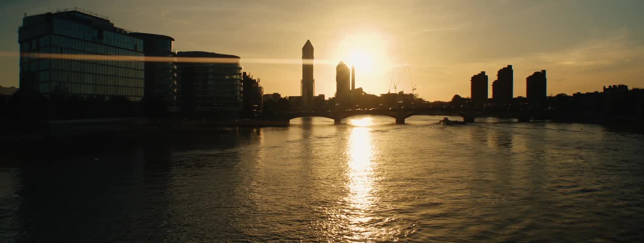 A sunset over london with the sun casting a golden glow on the river thames and silhouetting the cityscape including iconic landmarks like the shard and waterloo bridge