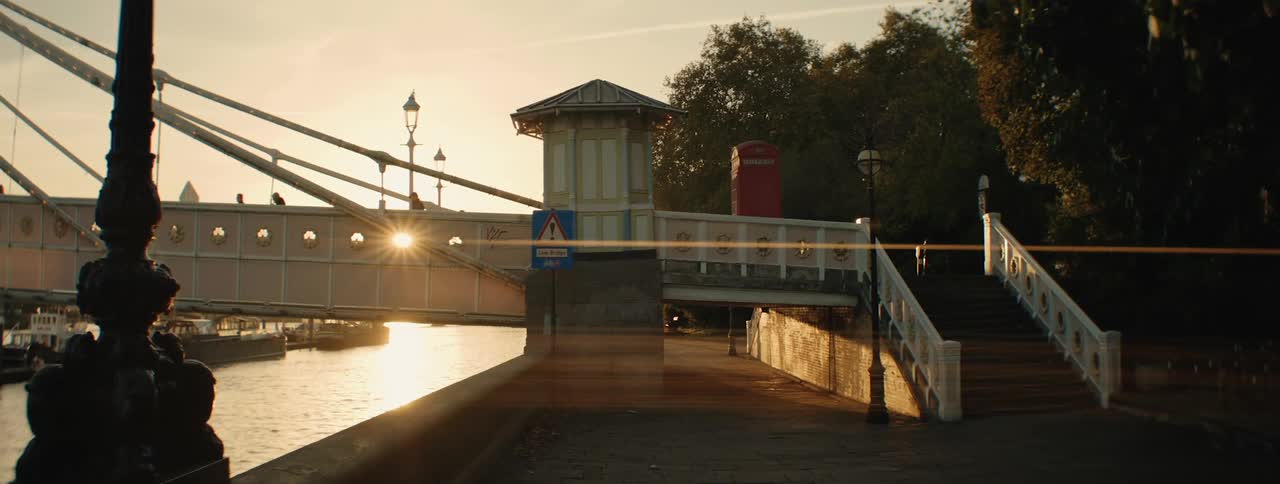 A pedestrian walkway along the river thames at sunset with a bridge and boats visible in the background
