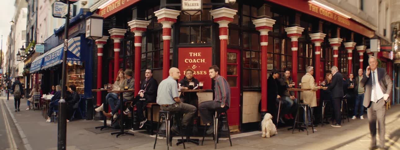 People sitting outside a corner bar in a metropolis