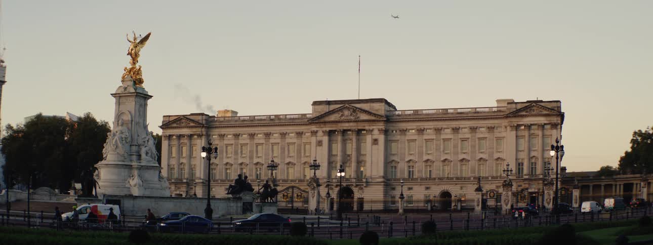 Buckingham palace stands with the victoria memorial in the foreground and a plane flies in the sky above