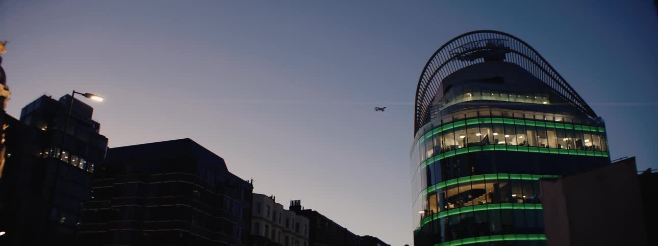 Modern buildings illuminated at night and a plane flying overhead