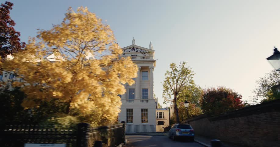 A stately historical building identified as the nash terraces in regents park london stands prominently on a sunny autumn day framed by vibrant yellow foliage from trees lining the street