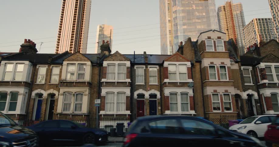 A row of traditional brick houses with a tall modern skyscraper looming in the background suggesting a contrast between old and new architecture in a city setting