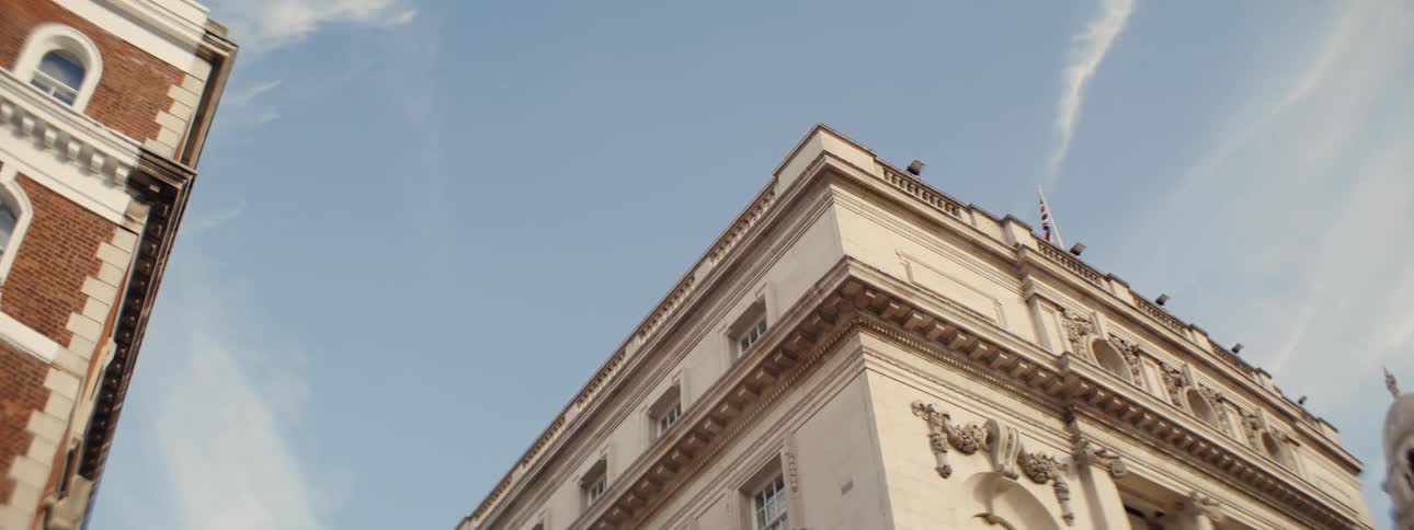 A lowangle shot shows the upper facades of likely government buildings in whitehall london as the camera moves suggesting a view from a moving vehicle