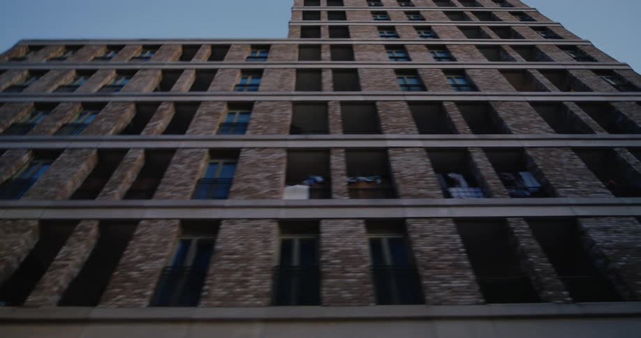A tall modern brick building with many windows viewed from a low angle against a clear sky