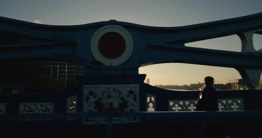 People crossing a bridge in the late afternoon with urban buildings in the background