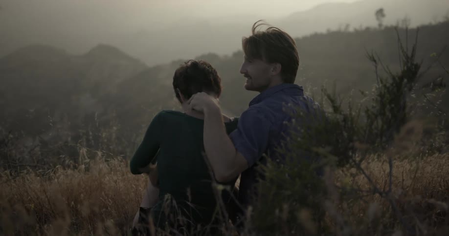 A man and woman with a small dog are sitting on a hillside and interacting