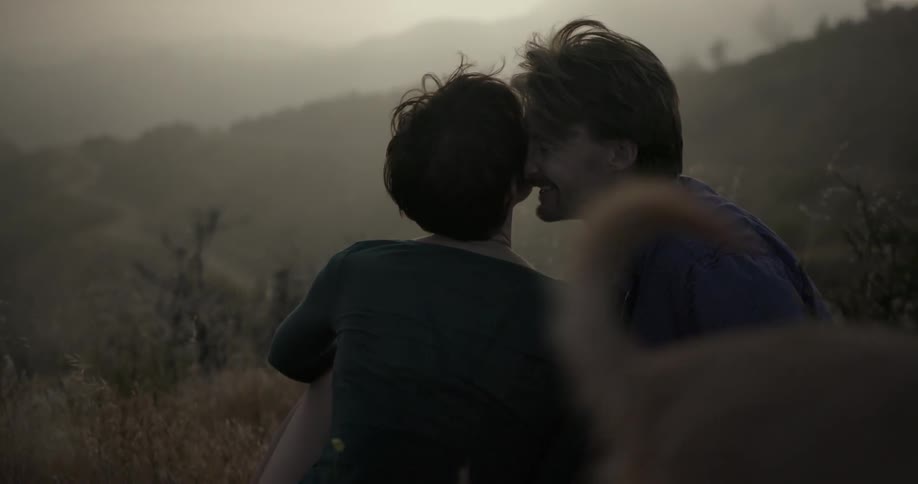 A man and woman cuddle on a hillside