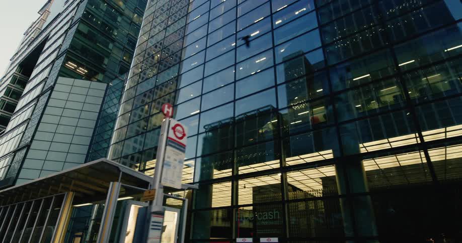 A low angle view of a modern skyscraper with a glass facade reflecting the surrounding buildings and a busy city street below
