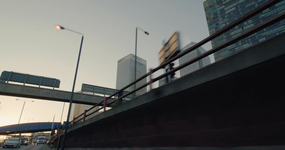 A view of several tall modern skyscrapers in the city of london with a bridge crossing over a busy street in the foreground