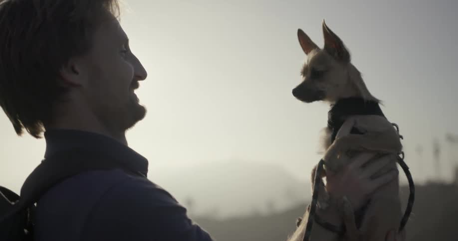A man is smiling as he is holding a small dog up in front of himself