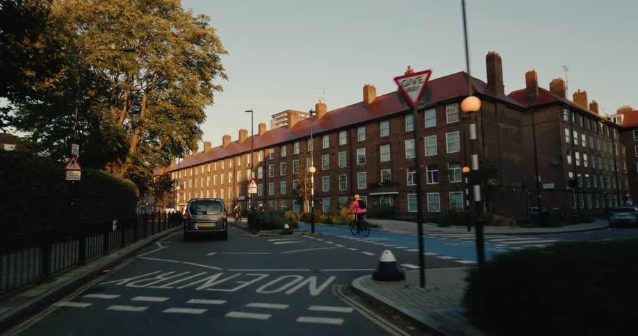 A cyclist rides along a dedicated bike lane in a residential neighborhood with traditional brick buildings lining the street