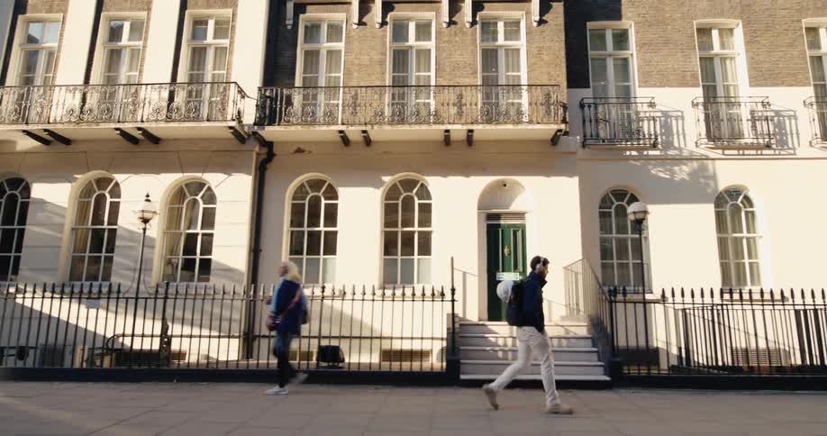 Two people walking on the sidewalk in front of a residential building